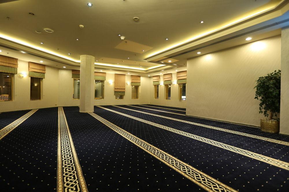 Makarem Ajyad Makkah Hotel Mecca Екстер'єр фото The photo shows a spacious indoor area with a plush blue carpet featuring a decorative pattern. The room is well-lit, with soft lighting along the ceiling. There are several windows, allowing natural light to enter, and a few plants are positioned ar