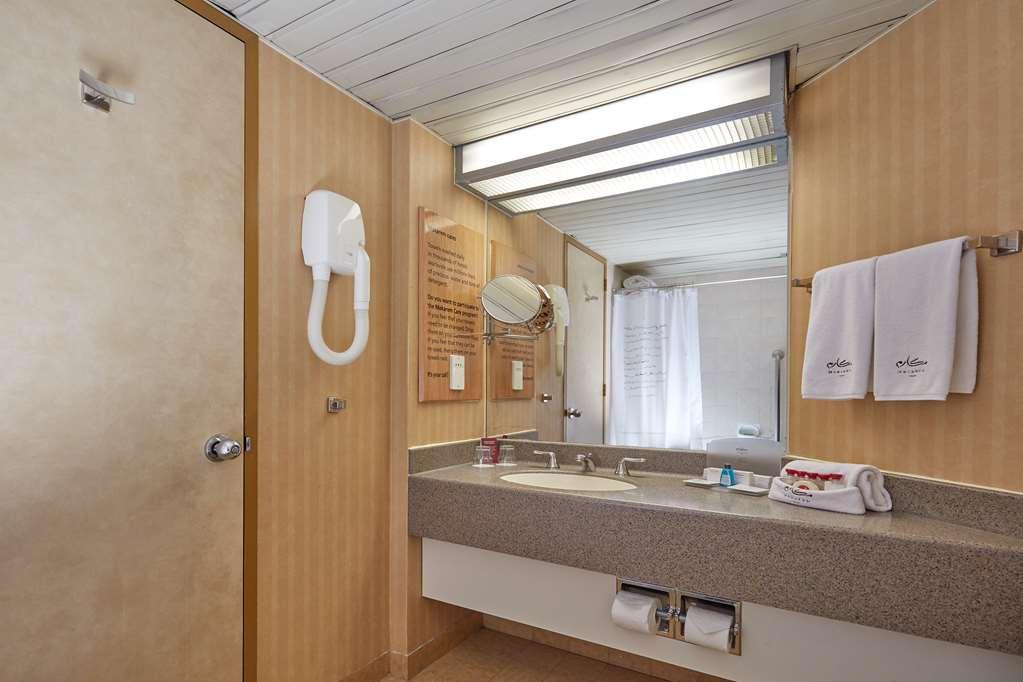 Makarem Ajyad Makkah Hotel Mecca Екстер'єр фото The photo shows the interior of a bathroom. It features a light-colored wall with vertical stripes and a ceiling that is white and textured. There is a gray countertop with a sink and a mirror above it. On one side, there are two white towels hanging