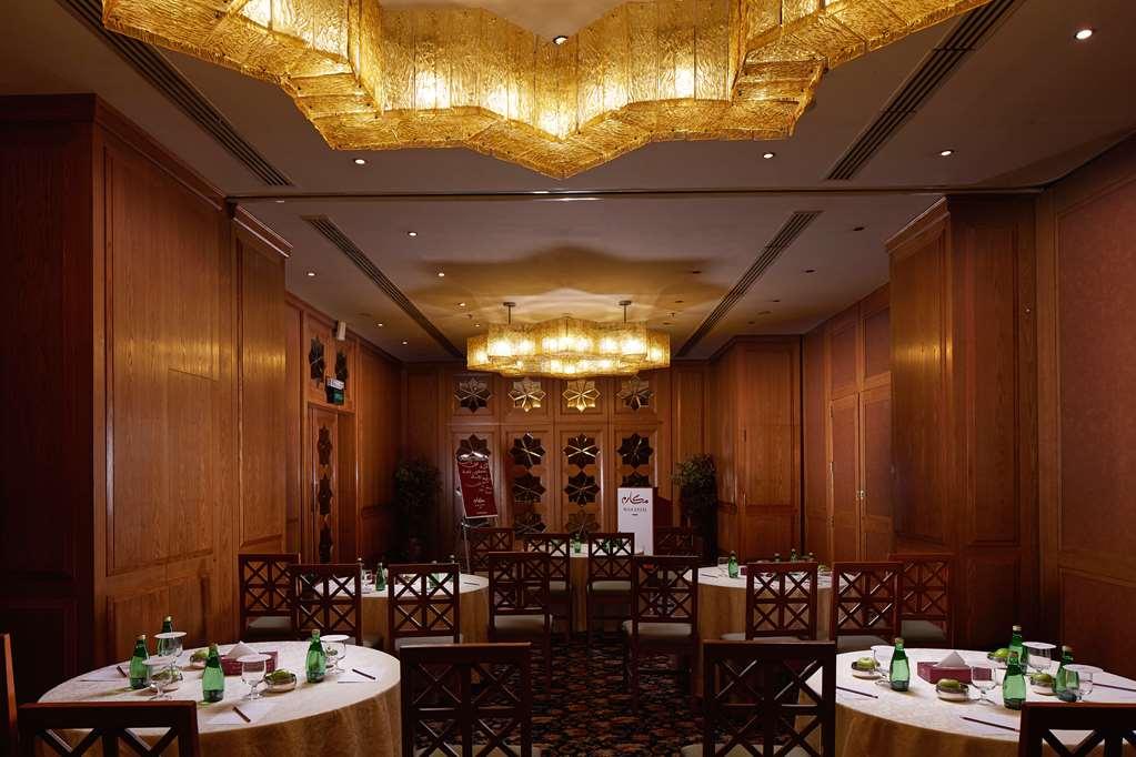 Makarem Ajyad Makkah Hotel Mecca Зручності фото The photo shows a well-decorated dining room with wooden paneling and elegant furnishings. There are round tables covered with tablecloths, and each table is arranged with glasses of water. The lighting is warm, provided by elaborate chandeliers on t
