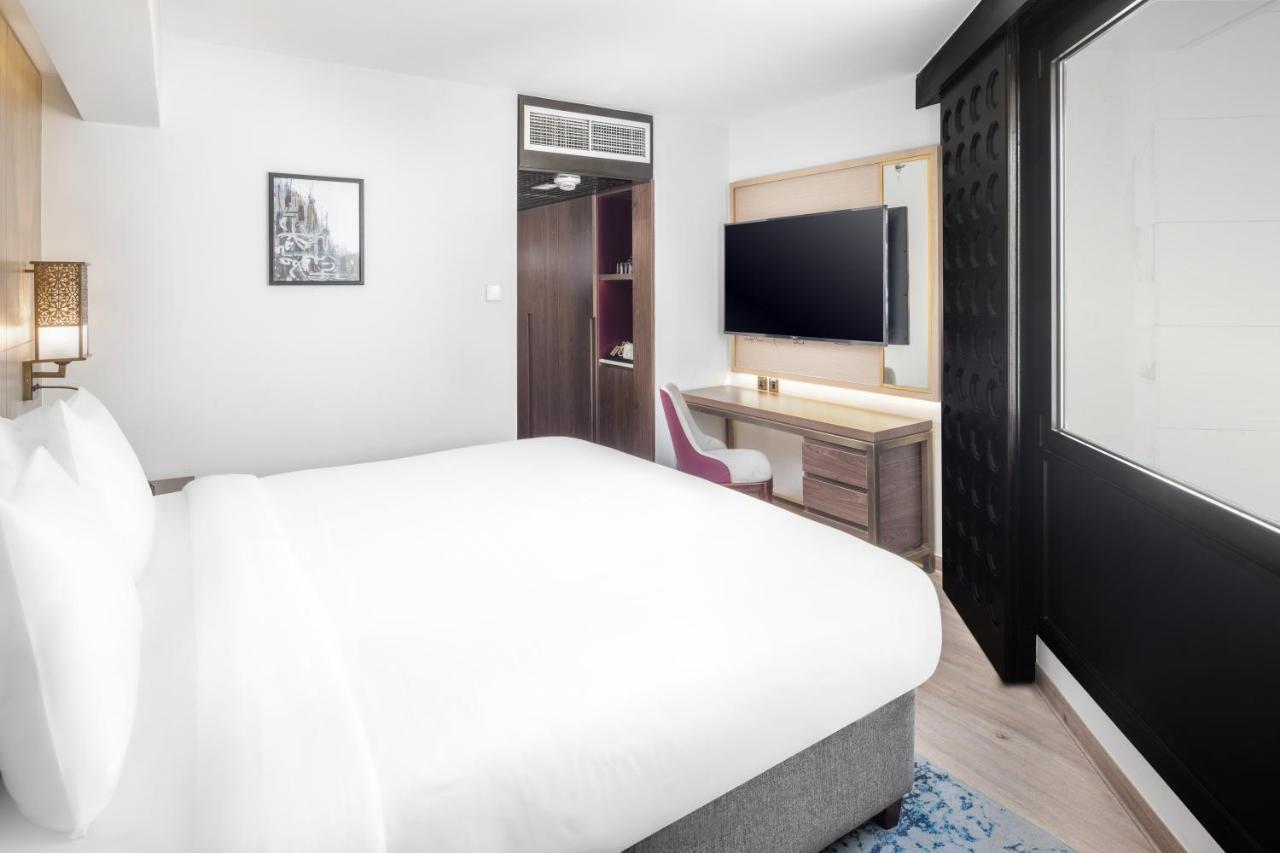 Makarem Ajyad Makkah Hotel Mecca Екстер'єр фото The photo shows a modern hotel room featuring a large bed with white linens at the forefront. In the background, there is a wall-mounted television across from a desk with a chair. A wardrobe or cabinet is located to the side, and there's a decorativ