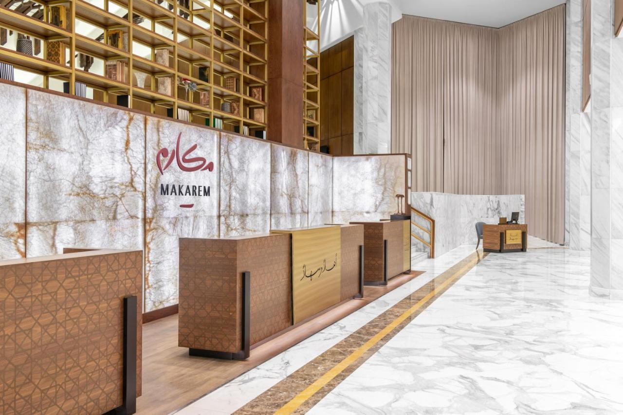 Makarem Ajyad Makkah Hotel Mecca Екстер'єр фото The photo shows a modern hotel reception area with a sleek design. The reception desk is made of a combination of wood and stone, featuring a warm color palette. The backdrop is adorned with a marble finish, giving a luxurious feel. Above the desk, t
