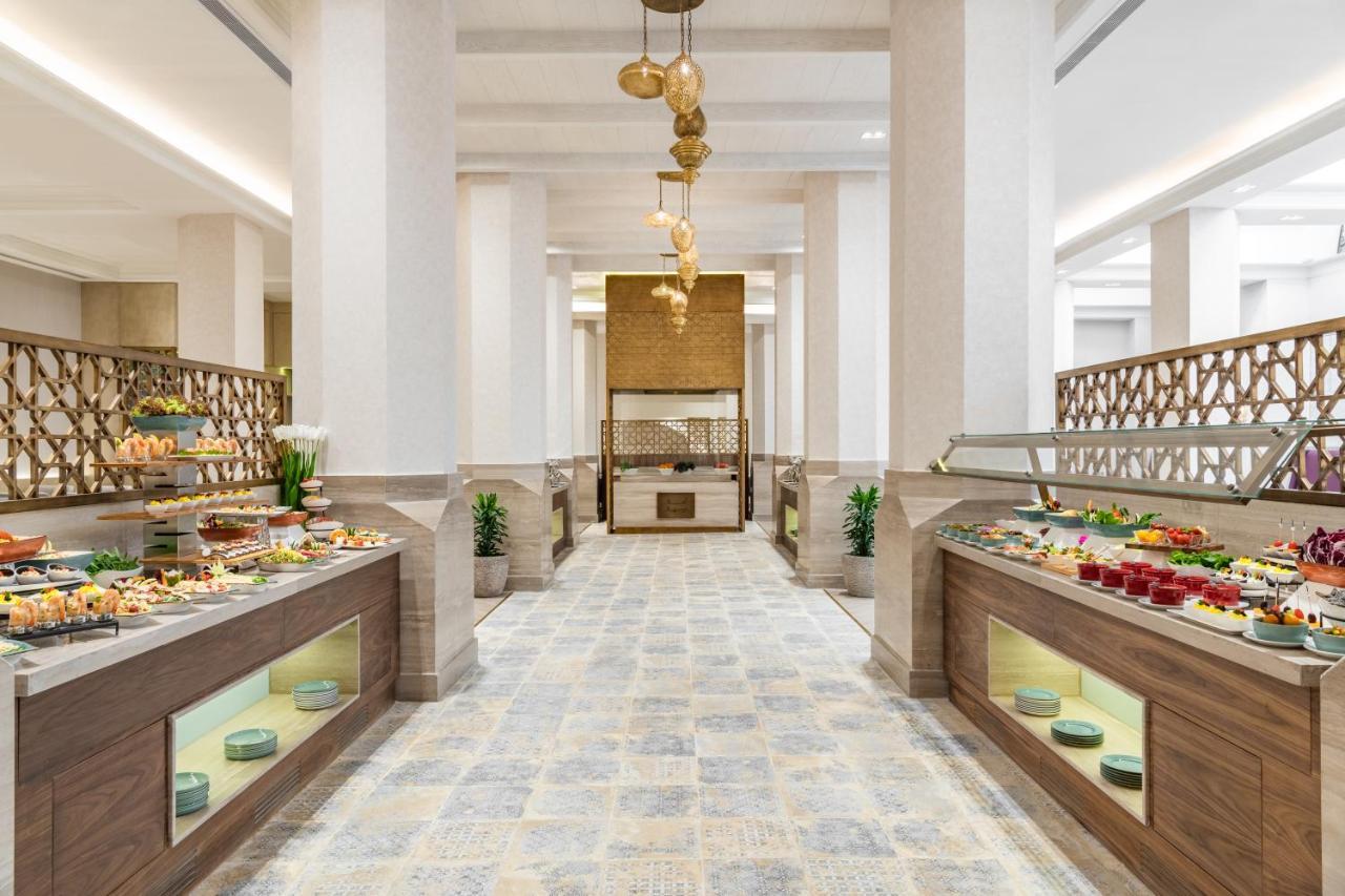 Makarem Ajyad Makkah Hotel Mecca Екстер'єр фото The photo shows an elegant restaurant or buffet area. There are two long buffet tables on either side, displaying a variety of colorful dishes and desserts. The tables have an organized layout and are adorned with small plants. In the center of the r