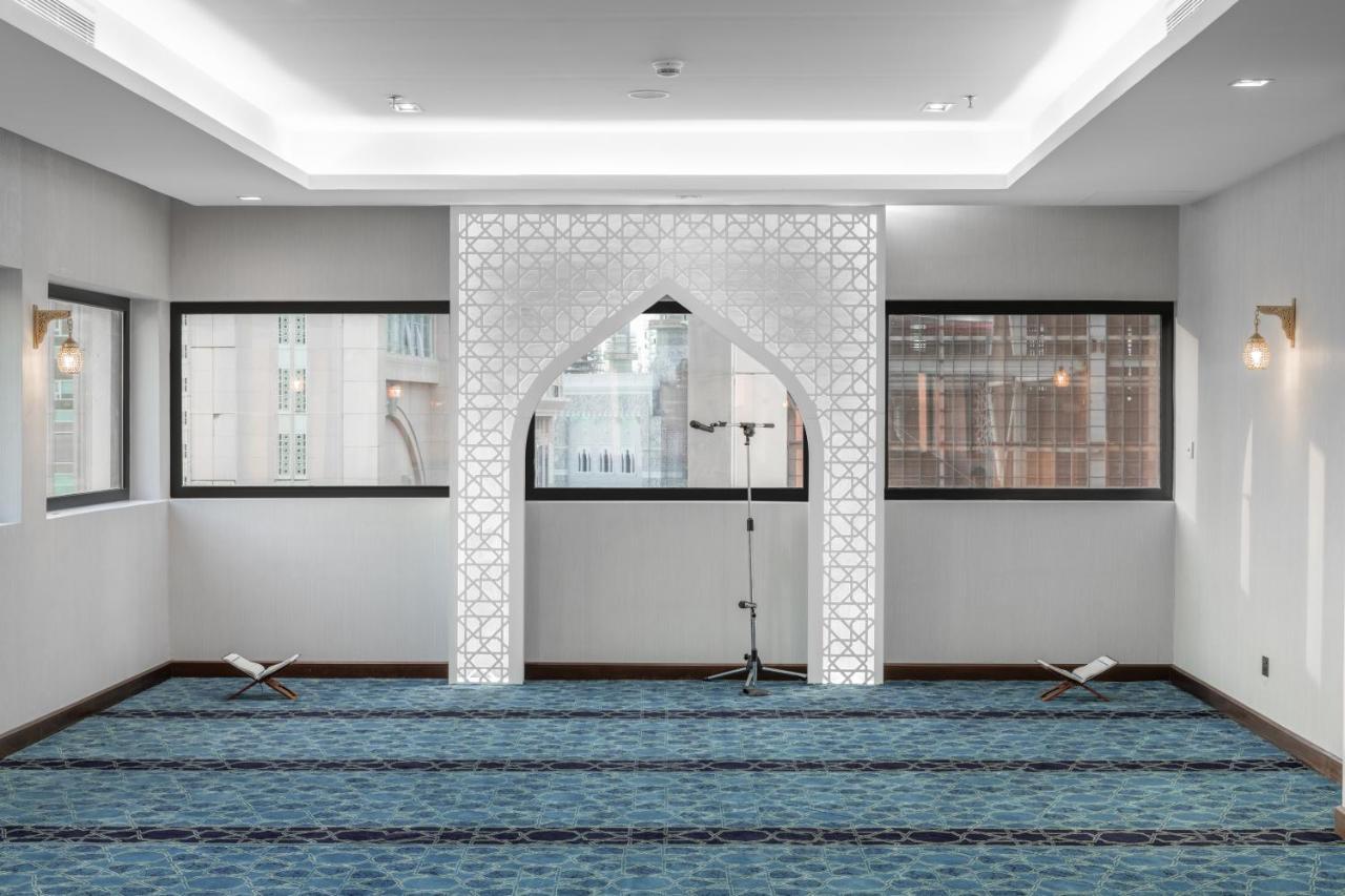 Makarem Ajyad Makkah Hotel Mecca Екстер'єр фото The image shows a prayer room or small mosque interior. It features a white decorative wall with an archway that is typical in Islamic architecture. The floor is covered with a blue carpet, arranged with patterned lines, likely indicating prayer spot