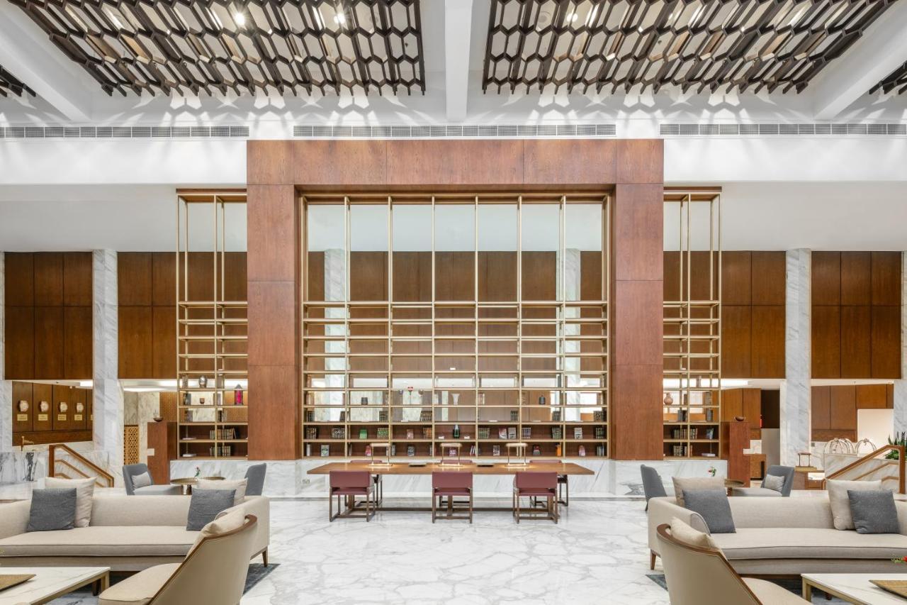 Makarem Ajyad Makkah Hotel Mecca Екстер'єр фото The photo shows a spacious interior of a modern lobby or lounge. The design features a large wooden structure with a grid-like pattern in the center, possibly serving as a decorative partition. The walls are adorned with brown wooden panels, and marb