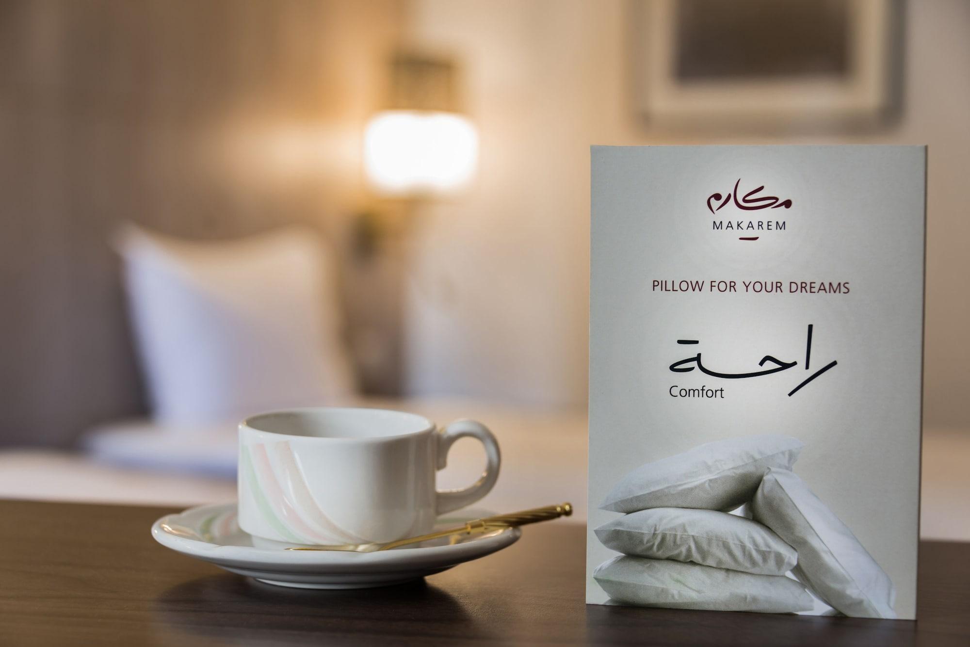 Makarem Ajyad Makkah Hotel Mecca Екстер'єр фото The image features a cozy setting, likely a hotel room. In the foreground, there is a white cup of coffee or tea placed on a small saucer, accompanied by a gold spoon. Beside the cup is a decorative card or sign that reads "Pillow for Your Dreams" an