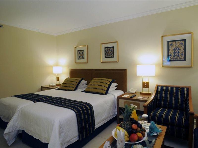 Makarem Ajyad Makkah Hotel Mecca Екстер'єр фото The photo shows a hotel room with a cozy and inviting atmosphere. It features two beds with white linens and dark striped bedspreads. There are two bedside lamps providing warm light, and the walls are decorated with framed artworks. Beside the beds 