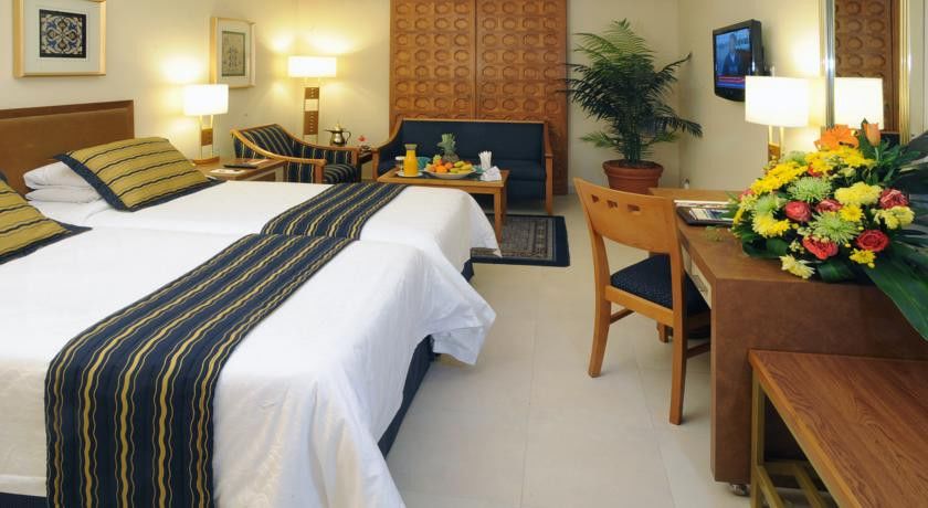 Makarem Ajyad Makkah Hotel Mecca Екстер'єр фото The image shows a hotel room featuring two beds with white linens and a decorative stripe along the edge. There is a seating area with two chairs and a small table, set with a breakfast spread that includes fruit and drinks. A small potted plant adds