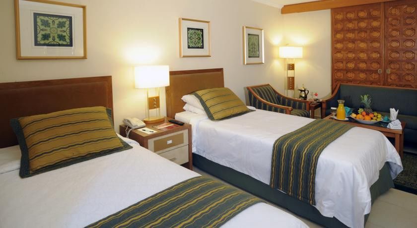 Makarem Ajyad Makkah Hotel Mecca Екстер'єр фото The photo shows a hotel room with two twin beds, each topped with decorative green and gold striped bed runners. There is a nightstand between the beds with a lamp on it. The room features light-colored walls, framed artwork on the walls, and a small